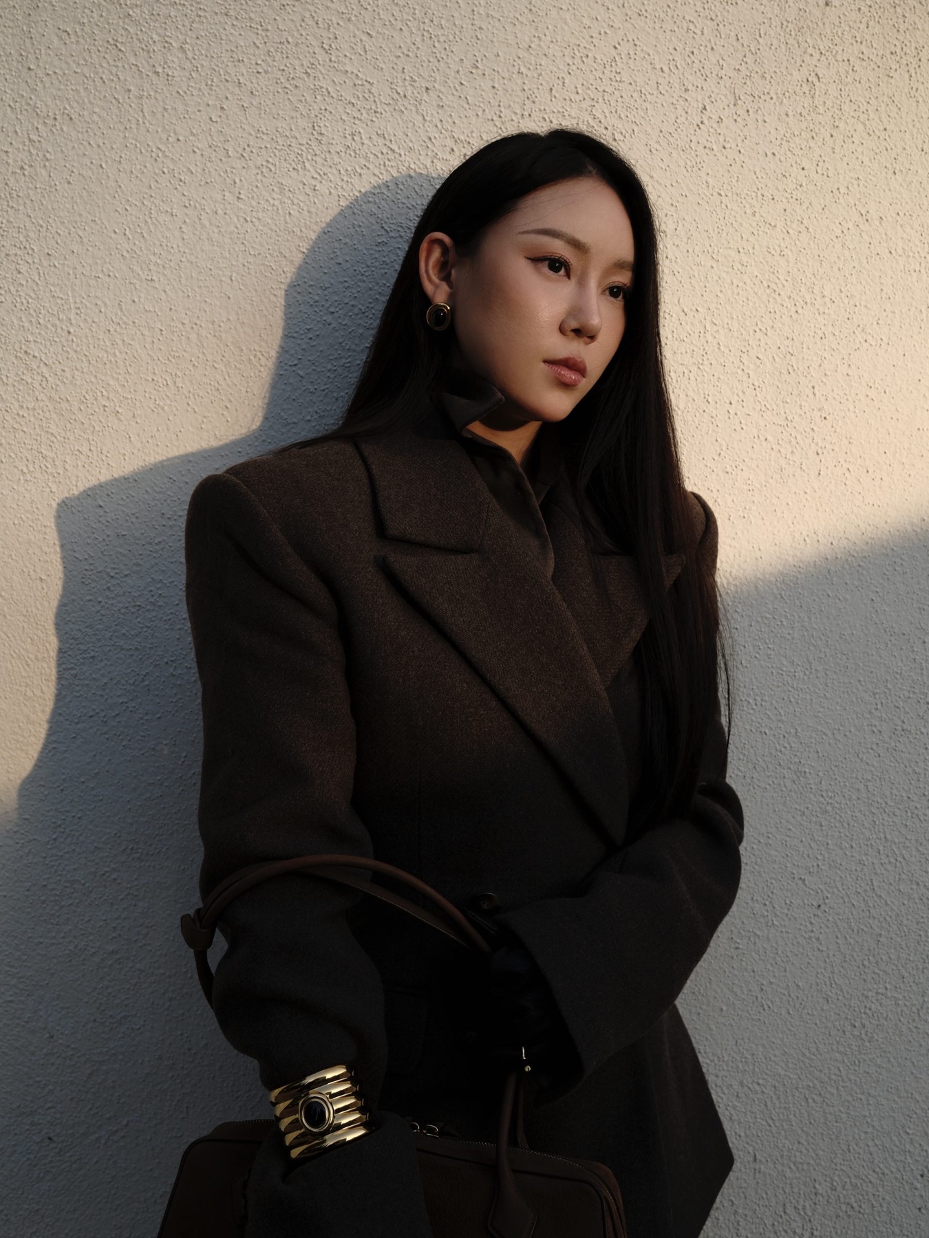 Brown tailoring in warm shadow against a pale wall