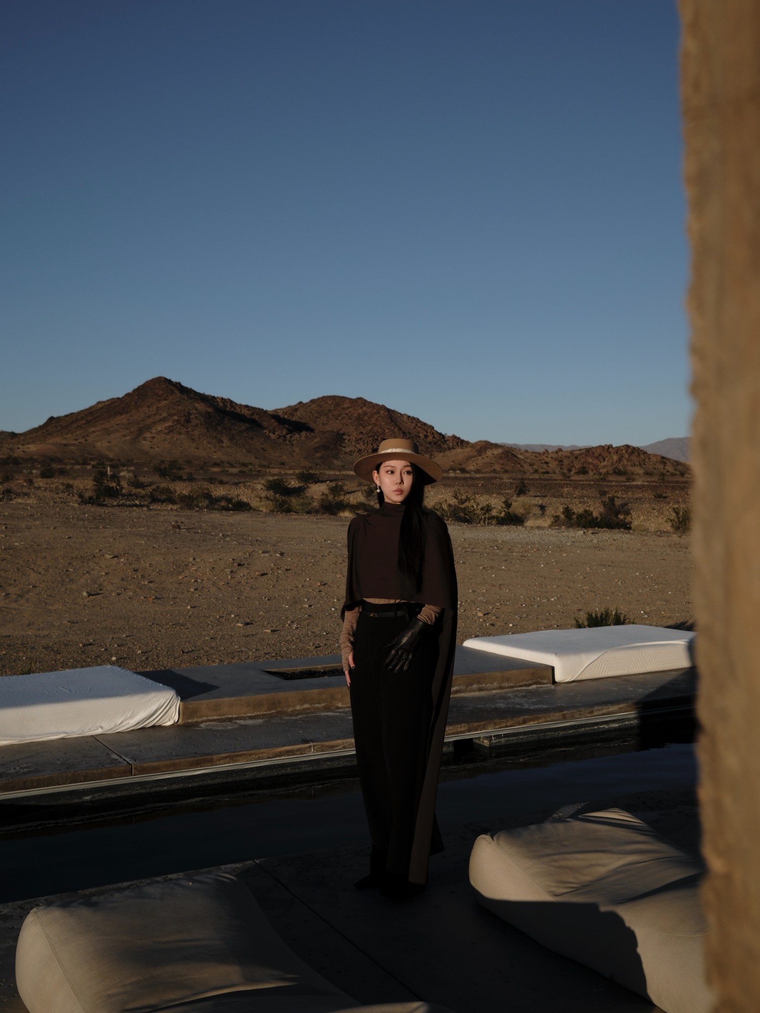 Wide-brim hat and dark tailoring against open desert at dusk