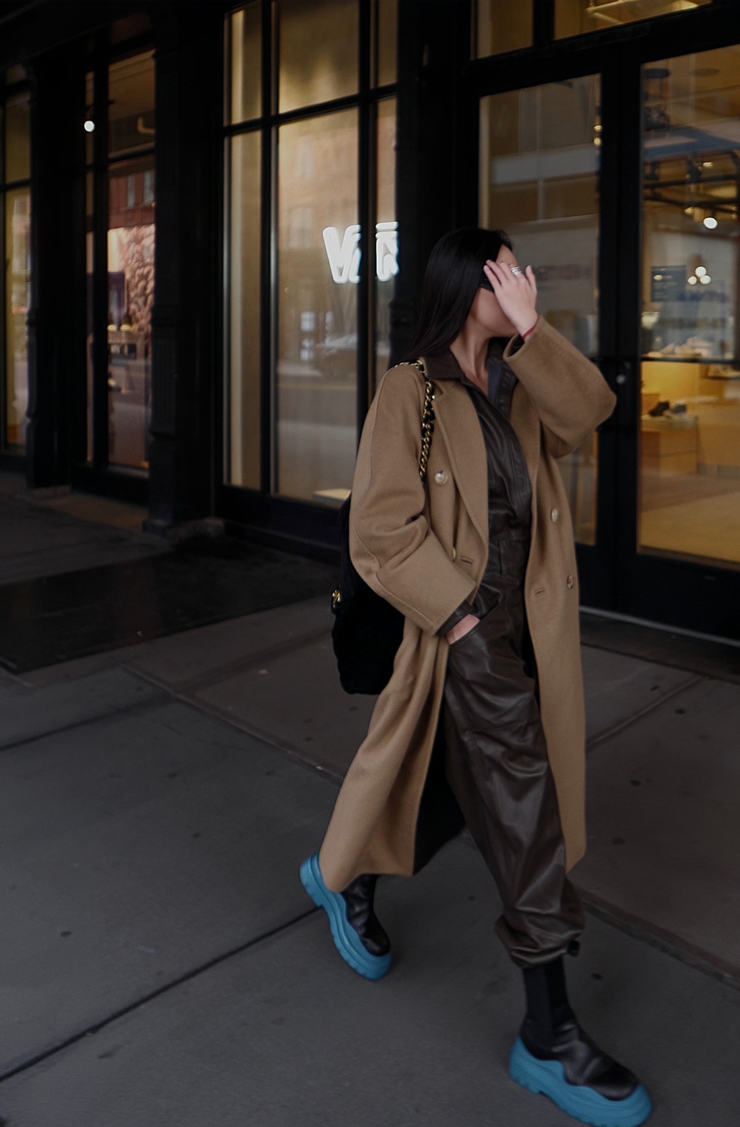 Leather one-piece worn under a camel coat with chunky boots on the street