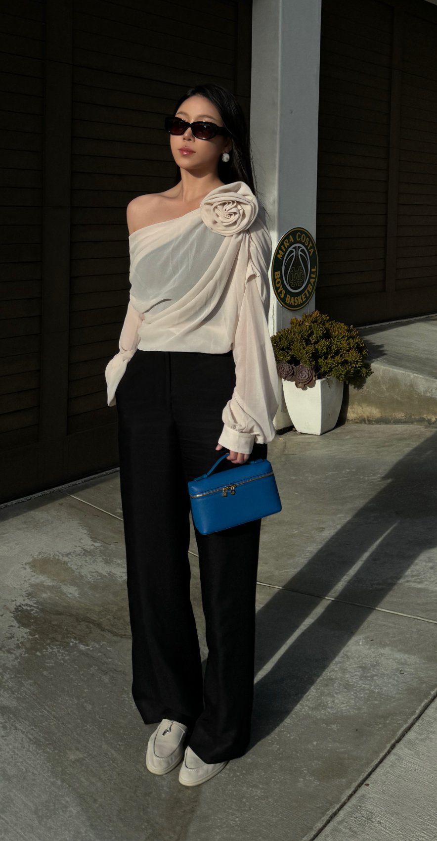 Commense rosette top and black tailoring with a blue mini bag, standing full-length