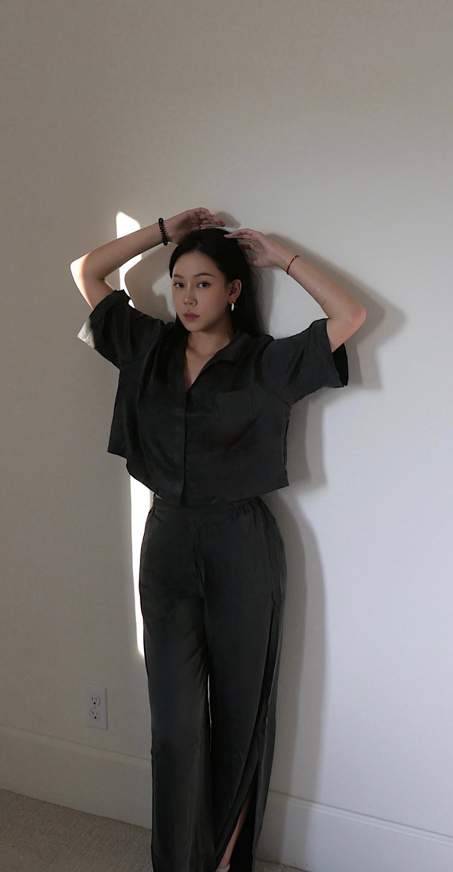 Lunya charcoal silk set with arms raised against a sunlit wall