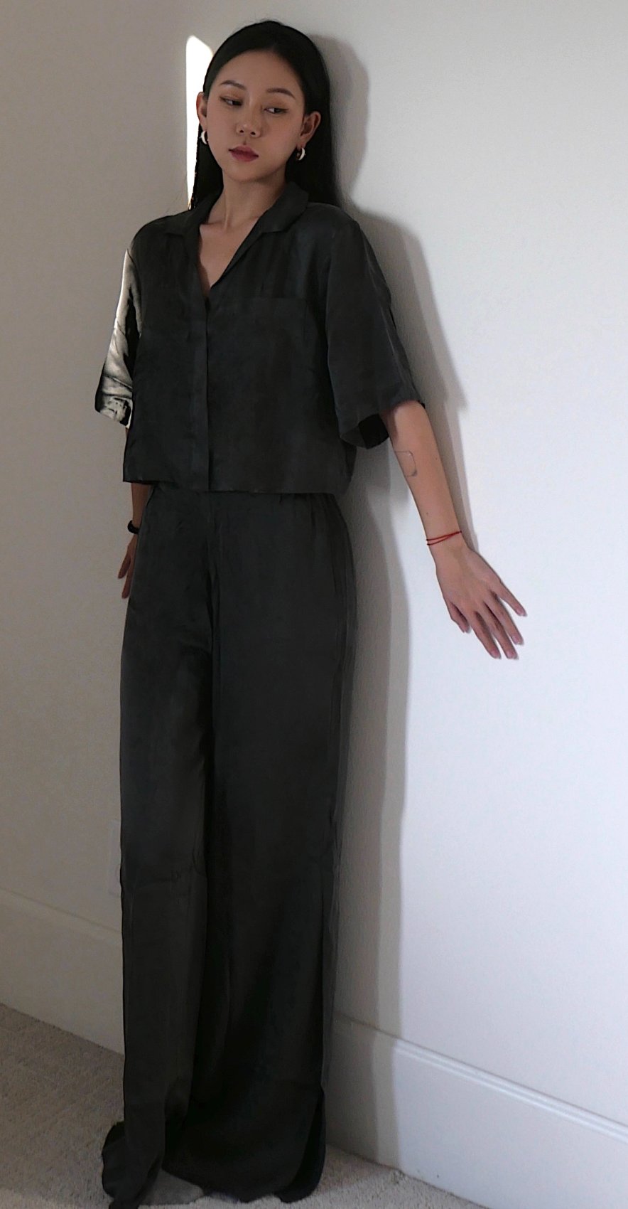 Lunya charcoal silk set resting against a white wall with arm extended