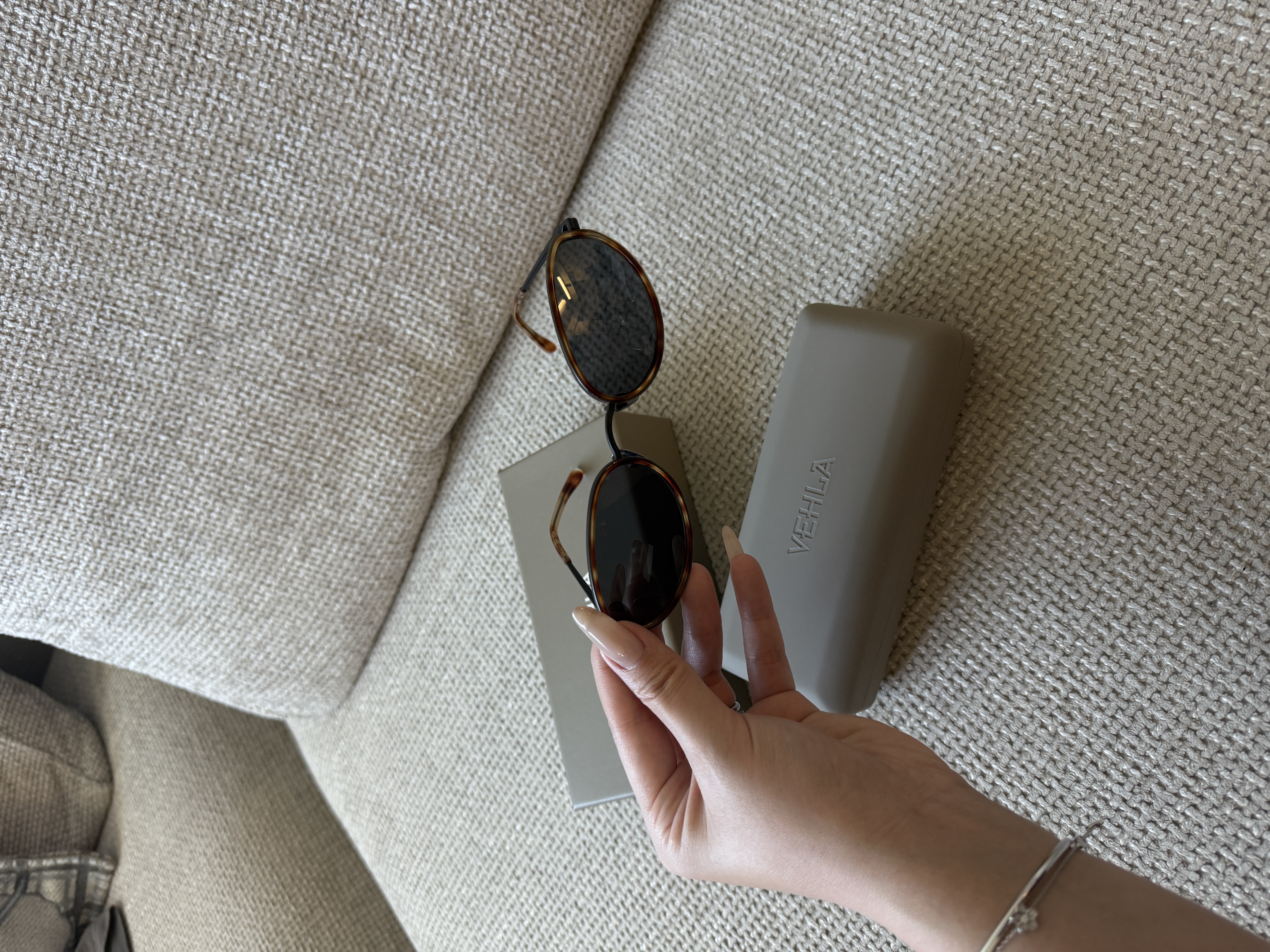 Vehla sunglasses and case arranged on woven upholstery